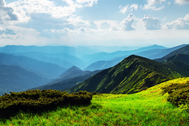 An image from a mountain overlooking several other mountains during midday with white clouds.